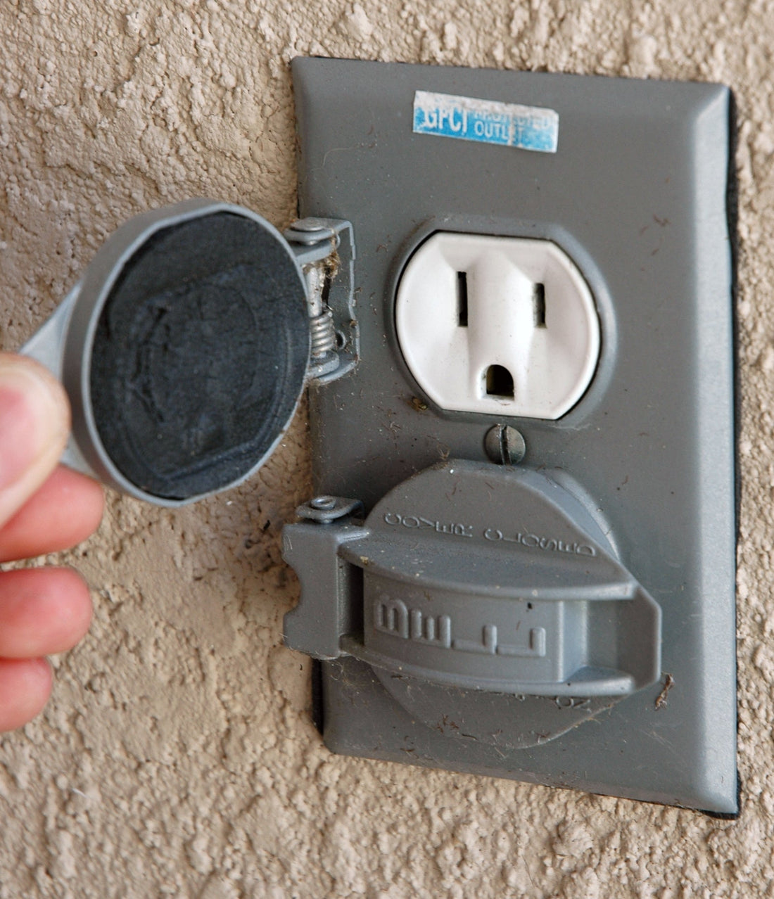A weatherproof outdoor electrical outlet with flip covers on the exterior wall of a house