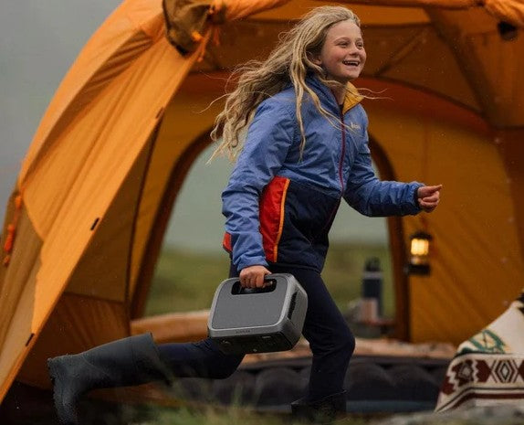 Child holding a portable power station in front of an orange tent