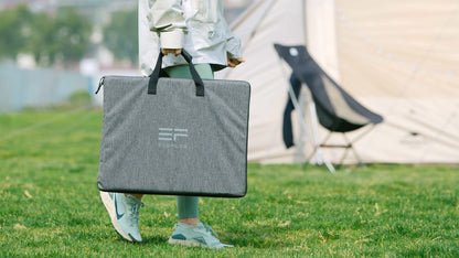 Person holding a gray carrying case with a logo, standing on grass near a tent.