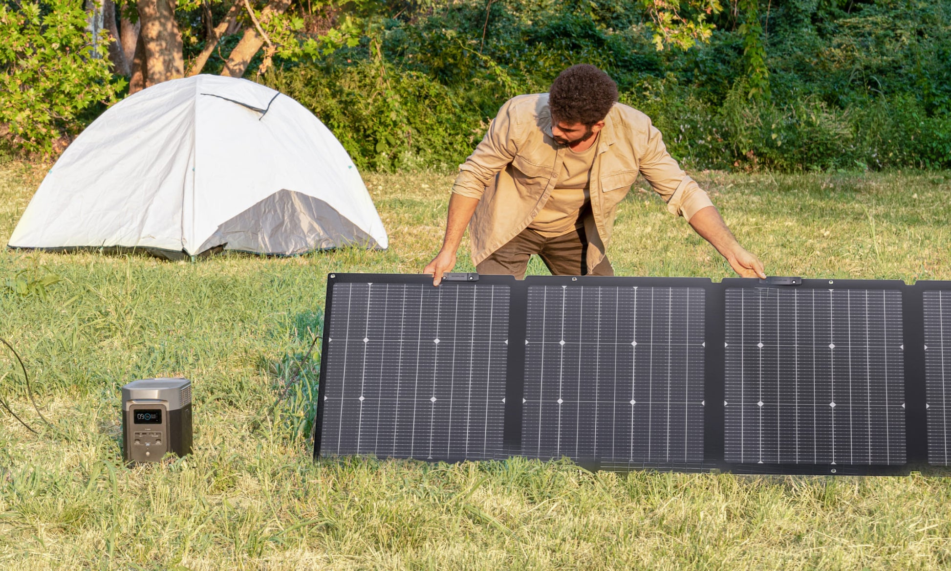 Person setting up a solar panel in a camping area with a tent in the background.